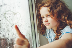 Happy child drawing heart on the window